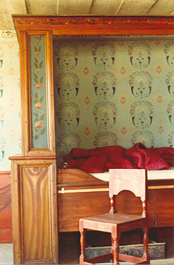 Skåp
                        sängen är kompletterad med en ny krönlist och
                        säng. Schablontapen är nygjord efter små
                        fragment som fanns kvar i huset, liksom
                        takbården måat med limfärg.